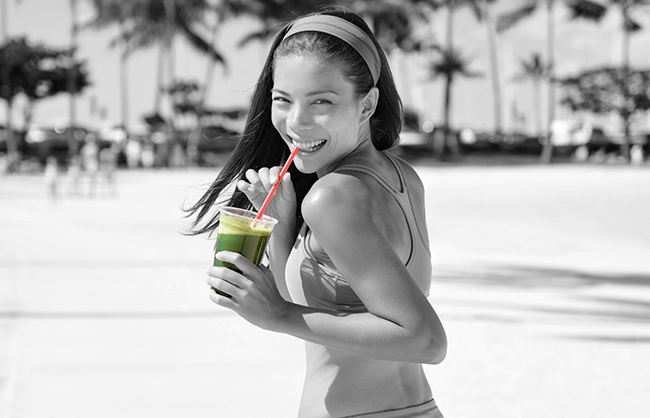 Lifestyle image of woman drinking green juice outside by palm trees